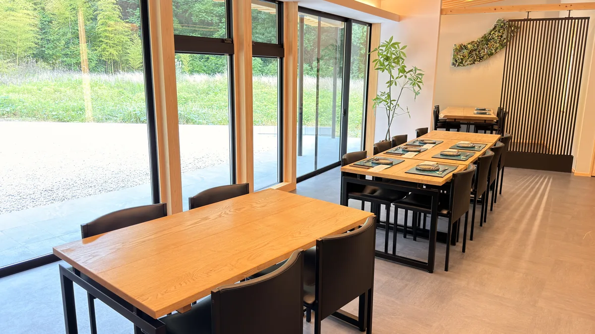 蕎席 雅山の店内。木のテーブル席と大きな窓、窓の外に庭と竹林が広がる客席