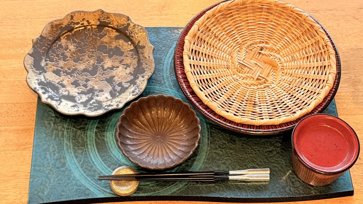 木のテーブルに蕎麦ざる・菊型の小鉢・金銀の皿・朱の蕎麦猪口を並べた雅山の器のセッティング